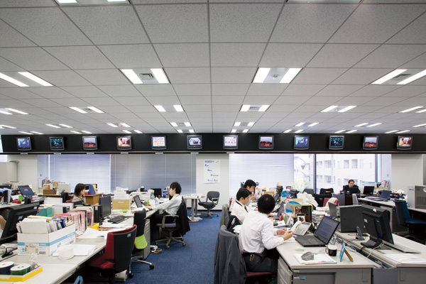 間仕切りのない開放的な執務スペース。 頭上にはテレビモニターがずらりと並ぶ